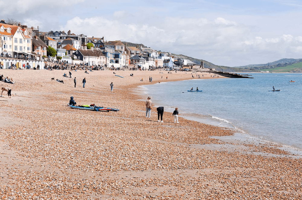 Scenic view of Lyme Regis on Lyme Bay, England, featuring a charming coastal town with traditional stone buildings, a pebble beach, and clear blue waters.