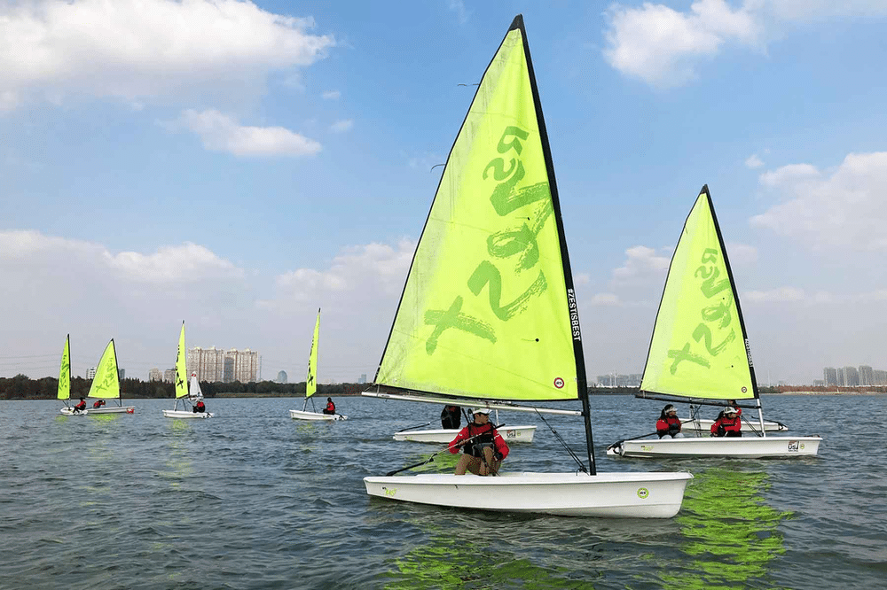 Group of people sailing on a sunny day, with vibrant bright green sails catching the wind. The boat glides smoothly across the sparkling blue water, surrounded by a clear sky.