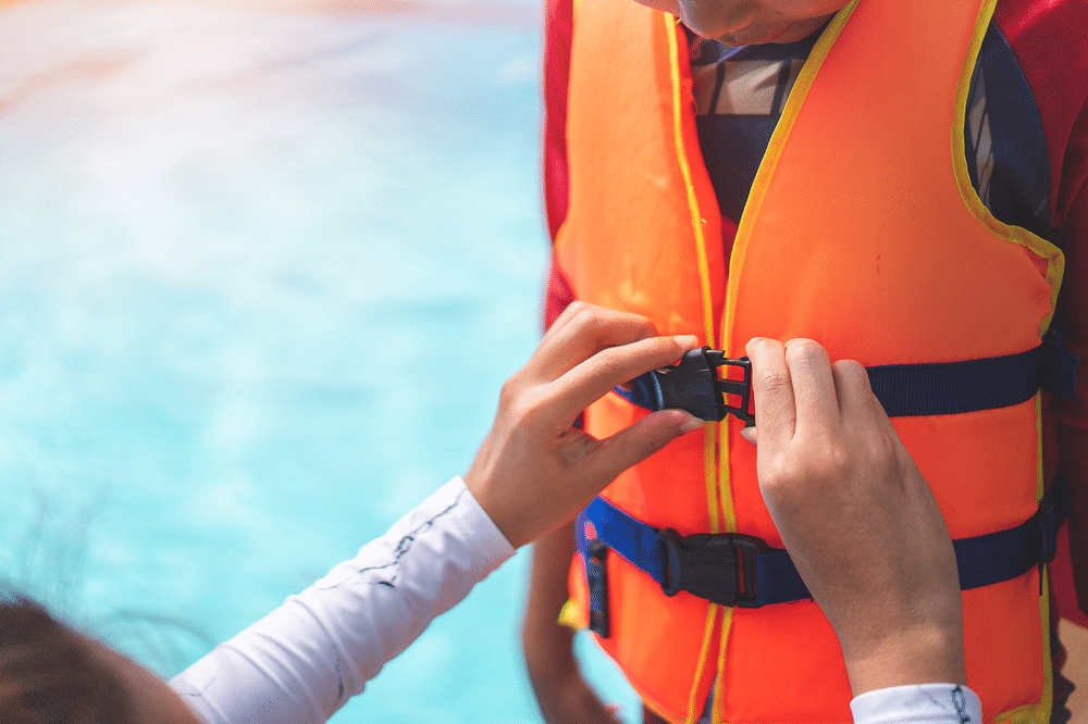 A person assisting another individual in putting on an orange life vest, ensuring a secure fit. 