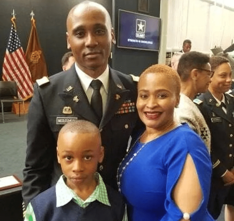 Darrell 'DJ' McCutcheon, Jr. stands proudly with his parents, Tamicia and Darrell McCutcheon Sr., at a ceremony. The family smiles together, dressed in formal attire.