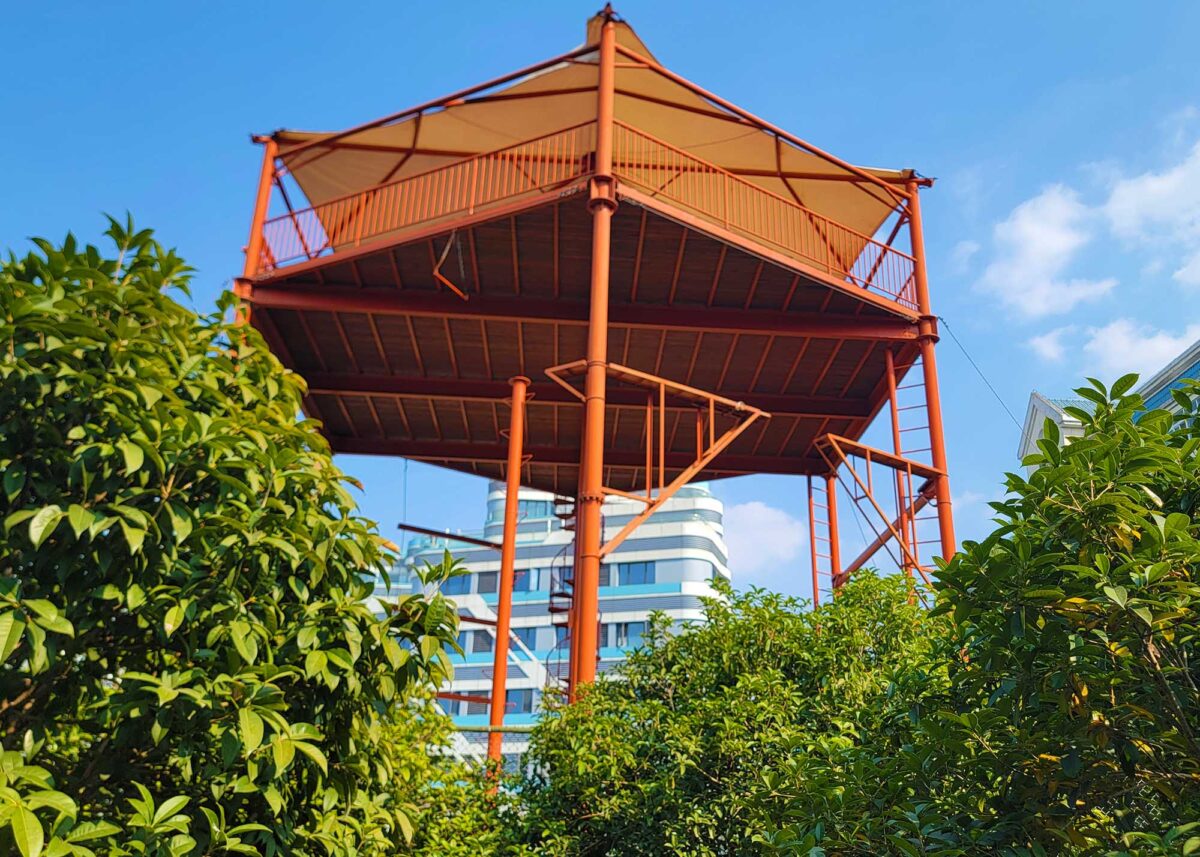 An orange challenge course located on the campus of Wuhan Sports University, designed for training students. The course is set against a backdrop of green trees and a clear blue sky.