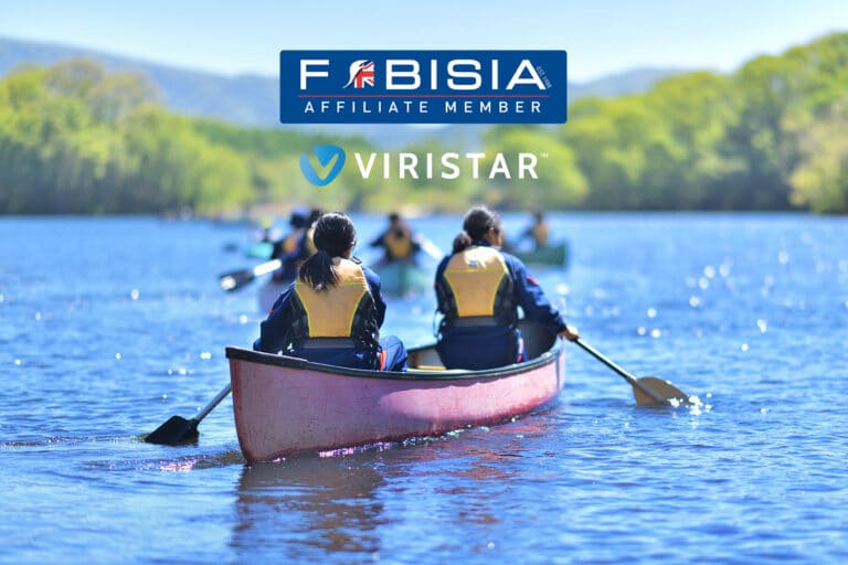 A group of people are paddling in canoes on a calm lake surrounded by green trees and distant mountains under a clear blue sky. In the foreground, two people wearing yellow life jackets paddle a red canoe. The FOBISIA Affiliate Member and Viristar logos are prominently displayed at the top of the image, signifying an affiliation.